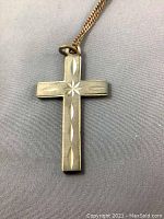 Close-up of cross pendant showing engraved star and oval pattern, gold tone finish