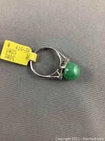 Side view of ring laid flat, showing jade sphere, band, and attached price tag.