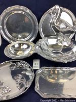 Six vintage pewter servingware pieces displayed on dark cloth background, showing general size, shape, and arrangement.