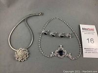 Photo showing two necklaces and four pairs of clip-on earrings arranged for display on a flat surface. The floral rhinestone pendant necklace is on the left, the filigree dark blue stone necklace is on the right, with the earrings above it.