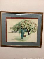 Full view of the framed print showing the woman walking under blossoming trees with vintage cars in the background. The frame is wooden with blue and red mats.