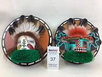 Two hand made Southwestern indigenous style wall-mounted masks with feathers and painted geometric designs, approx 9 inch diameter each.