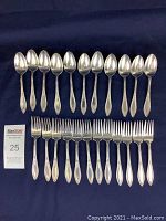 Photo showing 12 vintage spoons and 11 forks arranged on black background, all with matching ornate patterned handles, silver-tone finish, showing some surface wear