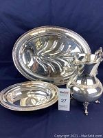 Three-piece silverplated servingware set on blue backdrop: oval serving tray, large pitcher with footed base, and matching serving bowl, showing tarnishing and wear.