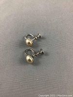 Two pearl screw-back clip-on earrings visible with cream-colored pearls and tarnished sterling silver backs.