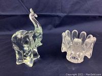 Two vintage clear art glass pieces displayed on a dark cloth background: a glass elephant figurine with a raised trunk, and a sculptural clear glass ashtray with an irregular shape.