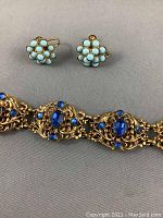 Close-up of gold plated bracelet with blue stones and earrings with white bead clusters