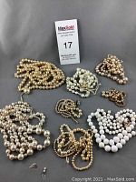 Full lot of eight vintage pearl costume necklaces laid out on grey background, showing variety in size, style, color, and condition.
