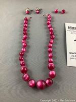 Pink pearl costume necklace and two pairs of matching pink pearl clip-on earrings displayed on gray surface, with identification card.