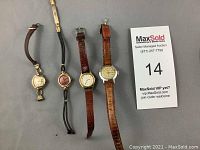 Four vintage ladies watches arranged on a flat surface showing varying strap types and dial colors.