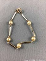 Top view of vintage bracelet laid flat showing pearl and gold-tone bar and chain link design