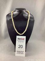 Single strand pearl necklace displayed on black bust with MaxSold auction card visible