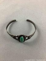 Front view of silver cuff bracelet centered on cloth background, showing turquoise stone and decorative silver bead border.