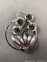 Front close-up view of the sterling silver floral brooch showing four roses and leaves on a circular frame.