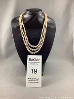 Three-strain pearl necklace on black display bust with lot card