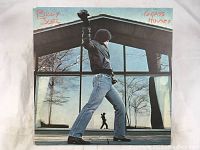 Front cover of Billy Joel Glass Houses vinyl album showing artist posing in front of glass house reflecting figure