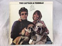 Front cover of The Captain & Tennille's Love Will Keep Us Together album featuring the duo and two bulldogs.