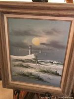 Full view of first oil on canvas painting featuring lighthouse, seagulls, dune grass, sun and ocean under wooden frame.