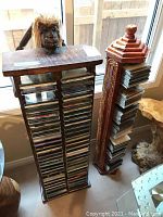 Two tall wooden CD stands designed as human figures with natural fiber hair holding racks of CDs