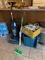 Photo of Dirt Devil vacuum, Swiffer mop, box of cords, and blue bin.