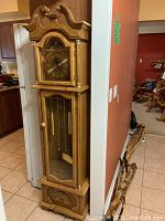 Full side and front view of a tall wooden grandfather clock with brass and glass features