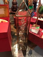 Glass display case with brass frame containing three Swarovski crystal figurines vertically arranged.