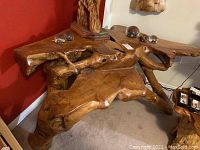 Front-angled view of the full two-tier teak root coffee table against red wall.