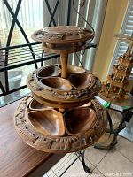 Side view of three-tier wooden revolving stand with carved serving compartments and detailed carvings around edges