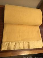 Folded buttery cream wool blanket with satin binding placed on wooden surface.