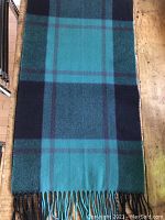 Full length view of the scarf spread out displaying the large checkered pattern in turquoise and black with muted red lines on a wood surface.