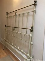 Full view of the antique cast iron and brass bed displaying the decorative leafy iron joins, brass rails, and finials.