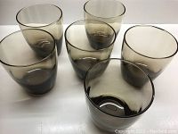 Set of six smokey grey/chocolate lowball glasses arranged on a white surface showing overall condition and color.