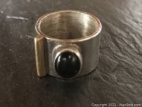 Front angled view of sterling silver wide band ring with black onyx stone and brass accent.