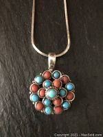 Close-up of circular pendant with alternating turquoise and coral stones set in sterling silver.