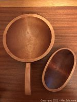 Two wooden nut bowls on a wooden surface. One larger round bowl with a handle and one smaller oval bowl.
