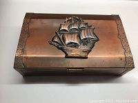 Top view of rectangular copper hinged box with hammered copper sides and raised copper tall ship decoration centered on lid.