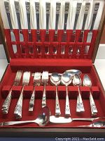 Overall view of stainless steel flatware arranged inside red felt–lined storage box.
