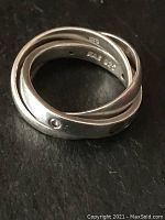 Close-up image of a vintage sterling silver Trinity ring with three interlocking bands; one band contains tiny embedded crystals. Inside is stamped 'FA 925'.