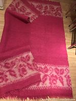 Full view of thick hot pink felted wool carpet showing one short edge with cream decorative border and wool fringe, laid partially rolled on wooden floor.