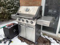 Front view of stainless steel Napoleon grill on deck with cover beside it