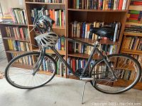 Full side view of the grey step-through Giant Cypress bicycle with flat tires, helmet and cable lock mounted