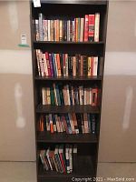 Full view of five-shelf dark wood bookshelf with multiple novels and books arranged vertically.