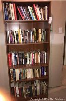 Full view of shelf unit with four shelves of books in mixed hard and soft covers.