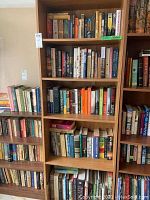 Wooden bookshelf with multiple shelves filled with various books, mostly novels and reference.