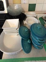 Set of glass and ceramic bowls and baking dishes including Denby, Corning Ware, Trudeau items arranged on kitchen counter.