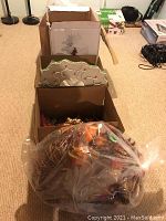 Photo of various boxed and bagged Christmas decorations placed on carpet, showing multiple items including wreaths and ornaments.