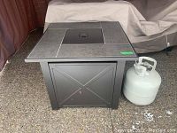 Front view of square fire pit table with propane tank beside it