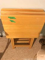 Three wood veneer folding tables stacked together showing top surfaces and folding legs, showing scratches and wear.