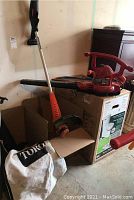 Toro red leaf vacuum and blower unit with collection bag and orange handle trimmer beside it.