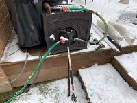 Full view of the dark brown self-retracting hose reel with green garden hose attached extending to the right and left, showing hose connected to spray nozzle and hose connectors.